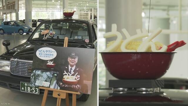 タクシーがまちの有名な食べ物の飾りを付けて走る